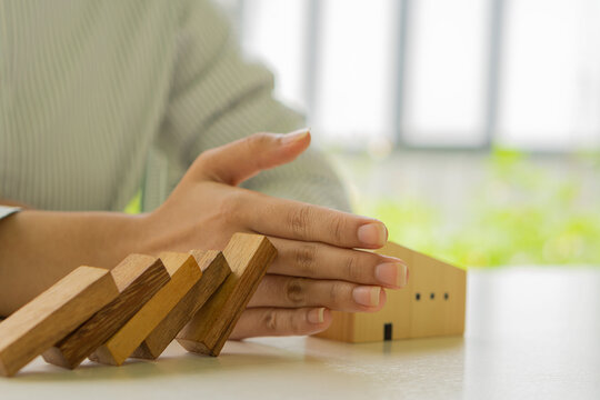 Woman's hand to stop risking a wooden block from falling. home insurance and safety concepts Financial protection stops the domino effect before it destroys the house.