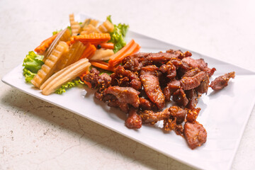 Close up deep-fried pork with sesame in beautiful white plate, side dish with pickled vegetables and fresh vegetable on a white stone table, Thai food menu