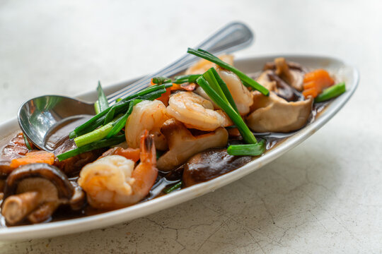 Stir-fried shrimps, Shiitake mushrooms, or Chinese mushrooms with oyster sauce in beautiful oval-shaped plate on the white stone table, close up image of healthy Thailand food menu.