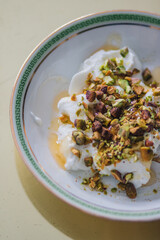 greek yogurt with honey and pistachios in white bowl with green and gold greek key