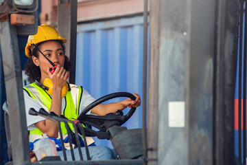 Female foreman use radio communication to communicate while driving forklift at shipping container...