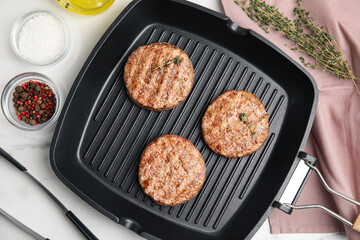 Grill pan with tasty fried hamburger patties and seasonings on white marble table, flat lay
