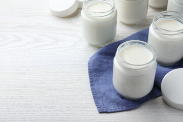Tasty yogurt in glass jars on white wooden table. Space for text