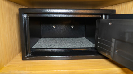 An open black empty safe with its door open in a wooden shelf. - obrazy, fototapety, plakaty