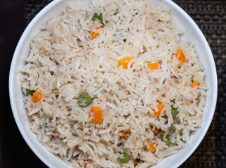 Top view of Vegetable Fried Rice in a white ceramic bowl on table mat background.