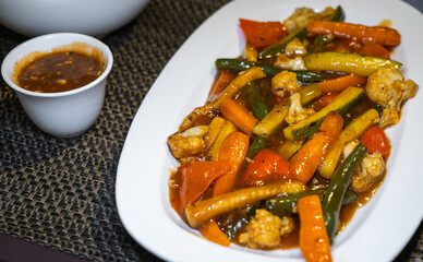 Sautéd exotic vegetables consisting of Zucchini, Baby corn, Broccoli, Beans, Carrots, Mushrooms, Cauliflower and Bell Peppers mixed in black pepper sauce and served in a white ceramic tray. 