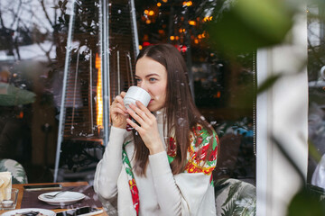 A young girl in a cafe is drinking tea, talking on the phone.