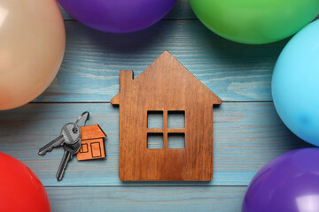 House model, keys, trinket and balloons on light blue wooden table, flat lay. Housewarming party