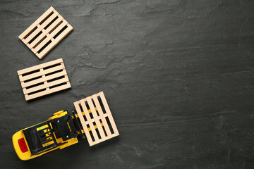 Toy forklift and wooden pallets on black table, flat lay. Space for text © New Africa