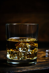 Glass chilled whiskey with ice cubes on wooden background in cellar.