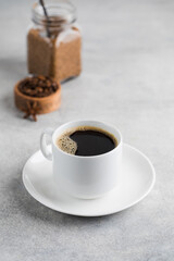 Black coffee in a white mug on a saucer on a grey table. Instant coffee.