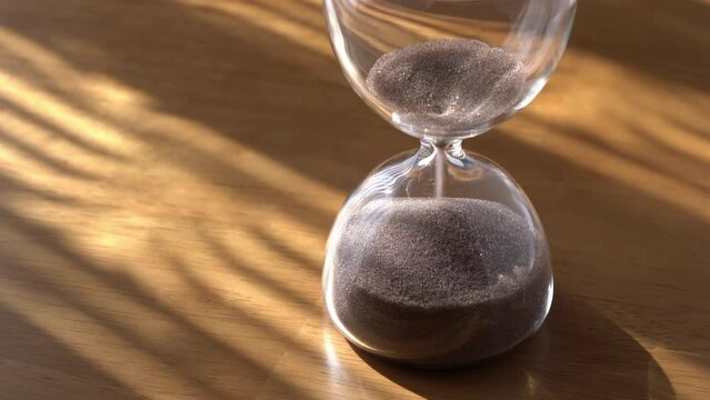 An hourglass on a wooden table. The sand falls to the end.