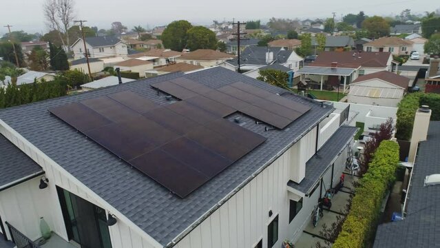 Slow aerial drone orbit right to left of the front of a house with solar panels installed on Los Angeles house rooftop on a cloudy day