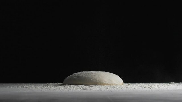 Baker dropping flour on bread dough on black background