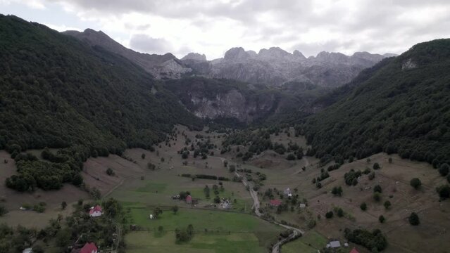 Drone video of the frontal plane advancing over the Lepush&euml; valley above the L&euml;pusha river, the sh20 in Albania, you can see small houses of the town, a somewhat cloudy sky and the dry river.