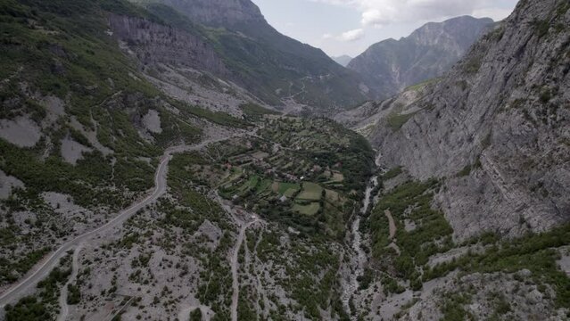 Drone video of a plane advancing from a bird's eye view on the Sh20 highway in Albania, at the height of Javor and Mreg with both towns in the scene, small houses of the town can be seen, cloudy sky.
