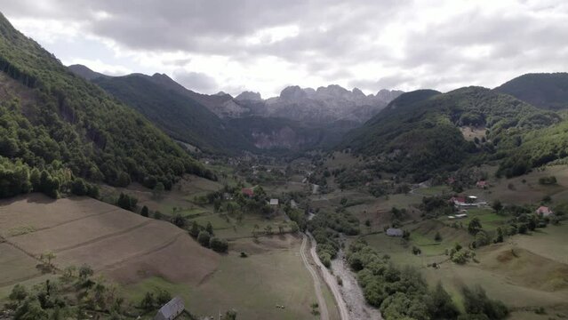Drone video of the frontal plane advancing over the Lepush&euml; valley above the L&euml;pusha river, the sh20 in Albania, you can see small houses of the town, a somewhat cloudy sky and the dry river.