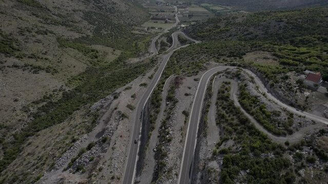 Drone video of frontal plane on the beginning of the mountain pass of the Sh20 highway in Bridje Albania, in the background you can see Lake Skadar, you can see houses of the town, winding road.