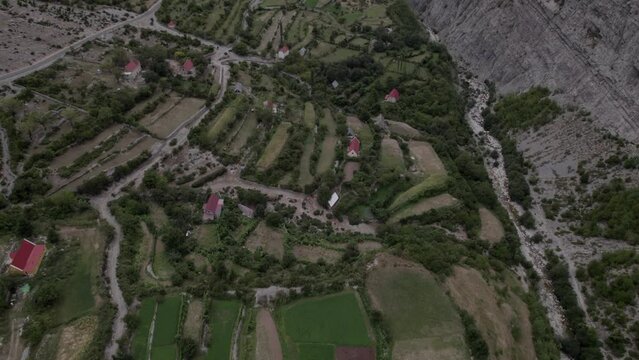 Video with descriptive panning Drone advancing on the Sh20 highway in Albania, at the height of Javor and Mreg, cloudy sky, houses in the village and farmland.