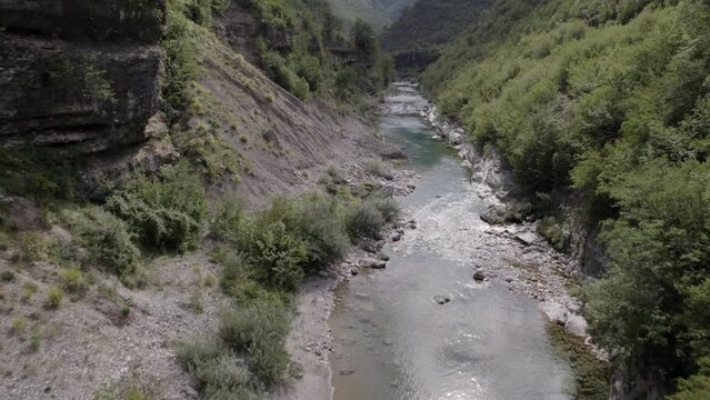 Drone video of ascending frontal plane advancing over the interior of the Cemi river on the Sh20 road between the mountains in Albania between Tamar&euml; and Selc&euml;, cloudy sky and turquoise river waters.