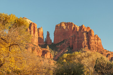 Naklejka premium The red rock formations reaching for the sky as the sun warms the stone and highlights the autumn leaves is a typical scenic landscape in the spiritual, beautiful Sedona, Arizona in western USA
