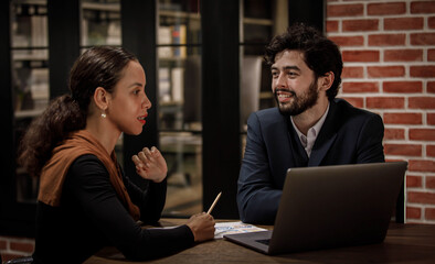 Caucasian successful professional bearded male businessman in formal suit sitting laughing smiling together with businesswoman colleague at meeting desk with laptop video call conference online