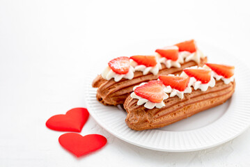 Eclairs with cream and strawberries on a white plate. Valentine's Day Concept