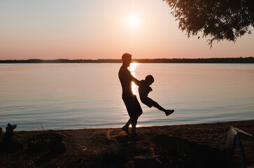 Happy family, father and son having fun together on beach at sunset in nature. Side view of dad holding child in arms against sky outdoors. Fatherhood, childhood