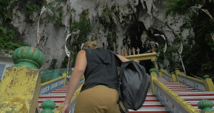 Young woman at Batu Caves, Malaysia climbs the stairs and takes pictures on tablet