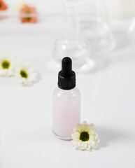 Bottle with skincare product and chamomile on wet surface and falling drops