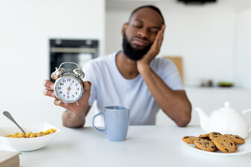 Black man suffering from insomnia holding showing alarm clock