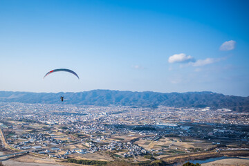 冬晴れの空を優雅に飛ぶパラグライダー。和歌山県紀の川市寺山スカイスポーツにて