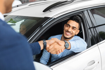 Cheerful arabic man sitting in new white car, shaking hand