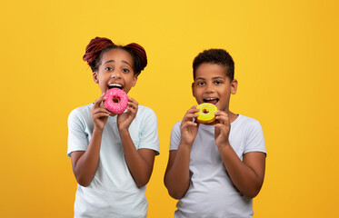 Happy black boy and girl eating delicious donuts