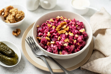 Beetroot salad with pickled cucumbers, walnuts, apple and mayonnaise in a bowl on a light gray kitchen table closeup