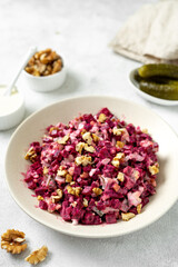 Beetroot salad with pickled cucumbers, walnuts, apple and mayonnaise in a bowl on a light gray kitchen table closeup