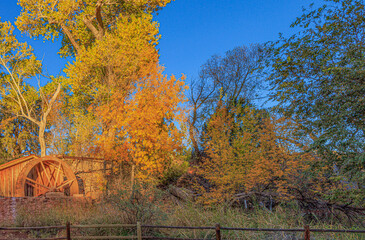 An old waterwheel from ages ago adds to the rural feel of this autumn image of colored foliage as the sun begins to set in this scenic capture in Sedona, Arizona in western USA