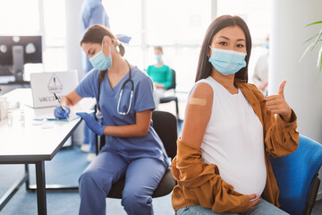 Vaccinated Pregnant Asian Lady Gesturing Thumbs-Up At Clinic