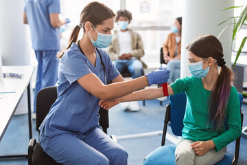 Teenage girl wearing face mask, nurse applying medical tourniquet