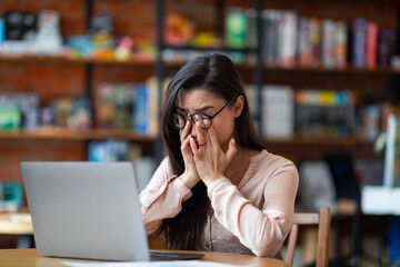 Exhausted female freelancer having eyesight problem while working on laptop in cafe, suffering from...