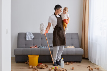 Full length portrait of Caucasian smiling man wearing brown apron cleaning apartment, washing floor...