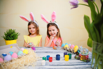Two cute child girls in bunnies ears paint and decorate Easter eggs. Preparing for Easter 