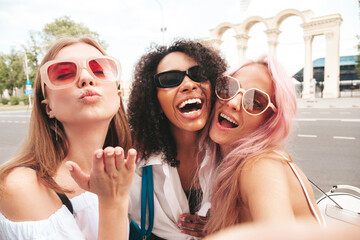 Three young beautiful smiling hipster female in trendy summer clothes.Sexy carefree multiracial women posing on the street background.Positive models having fun in sunglasses. Taking Pov selfie