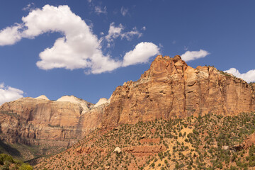 Zion National Park lies on the border of Arizona and Utah with a mix of high mountains of rock with green trees growing from the stone is scenic