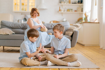 Happy mom relax on sofa in comfortable light living room, while cute boys sons play on warm floor,...