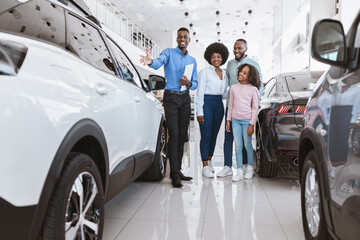 Car selling business. African American family consulting with salesman about purchasing new auto at...