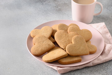 Valentine's Day breakfast, coffee with milk and heart shaped cookies on pink plate on gray background. Close up. Space for your greetings.