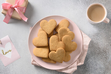 Valentine's Day breakfast with coffee, heart shaped cookies on pink plate and love blank on gray background. View from above.