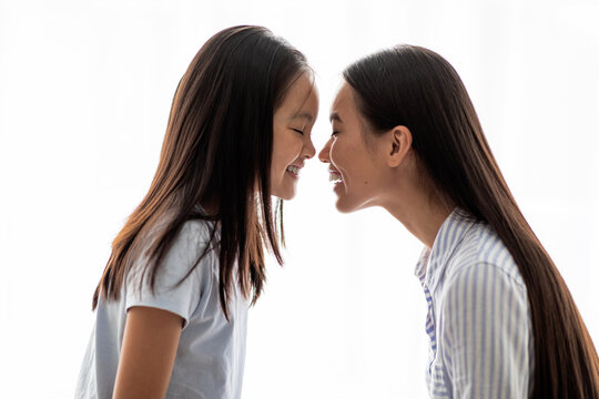 Loving Asian Mom And Daughter Touching Each Other With Noses Over White Background, Side View