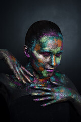 Young artistic woman in black paint and colourful powder. Glowing dark makeup. Creative body art on the theme of space and stars. Bodypainting project: art, beauty, fashion.